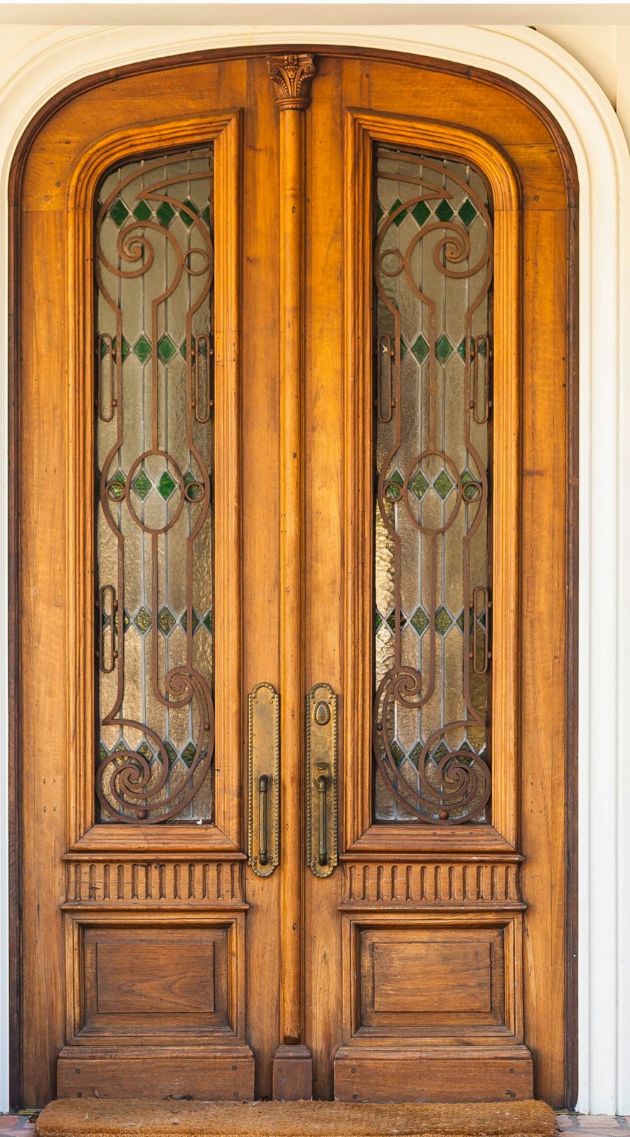 An elegant arched wooden front door with stained glass and brass handles